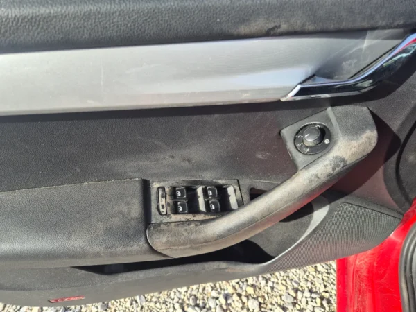 A close-up of the ŠKODA OCTAVIA 1.2 BENZIN/TNG’s dirty door interior shows worn window controls, door handle, and mirror knob, with sunlight highlighting the dust and grime.