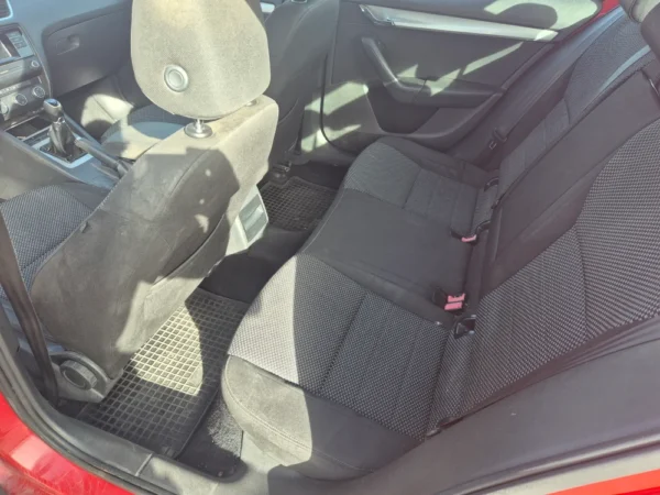 The image shows the clean, well-maintained backseat area of a ŠKODA OCTAVIA 1.2 BENZIN/TNG with black and gray fabric seats, black floor mats, and sunlight streaming in through the windows.