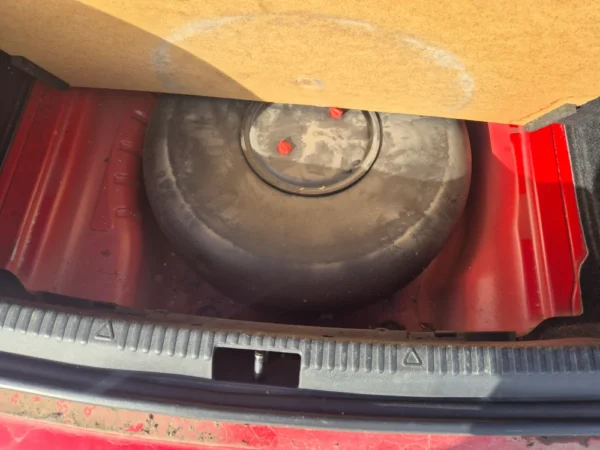 A close-up of the ŠKODA OCTAVIA 1.2 BENZIN/TNG trunk with the floor panel lifted, showing a round black spare tire secured in the well underneath.